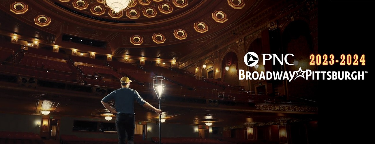 a screenshot from the 2023-2024 PNC Broadway in Pittsburgh teaser video of a man standing on the Benedum Center stage holding a light