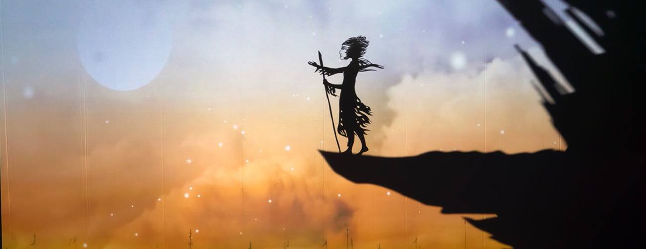 a paper silhouette puppet of a person stands on the silhouette of a cliff edge in front of a watercolor background