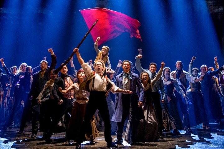 a group of people on stage with arms raised and a reg flag flying above them in the background 