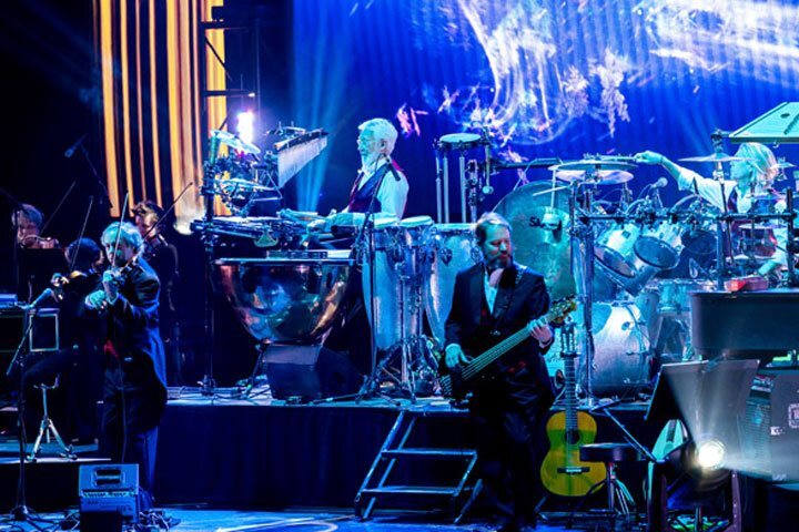 A violinist, two drummers, and a guitar player on stage.