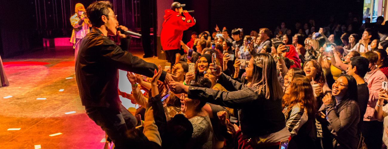 singer on stage reaches out an arm to touch the outstretched hands of people in the crowd.