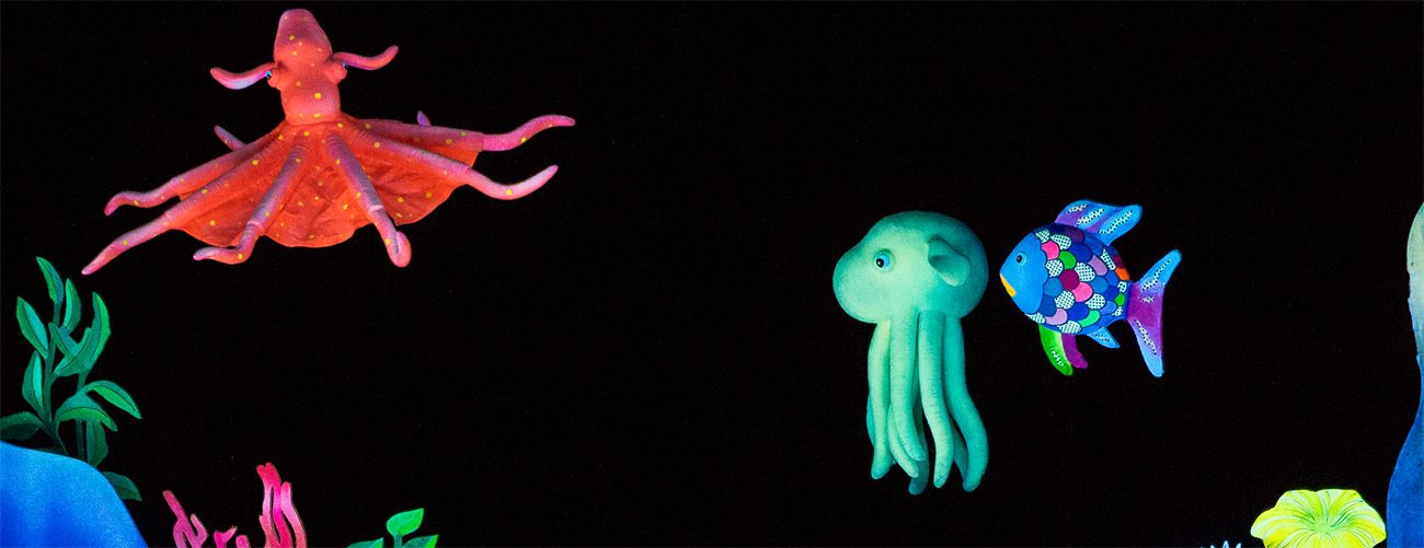 felt puppets of a red octopus, teal jellyfish and a rainbow fish float against a black background