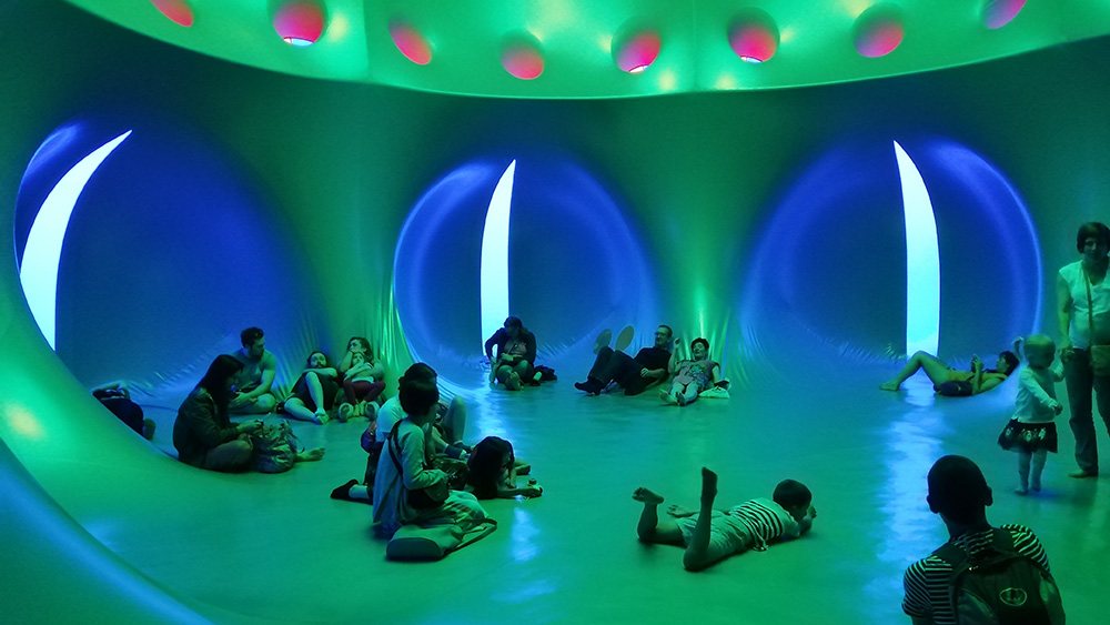 a group of people sit and stand in a large, green inflatable dome