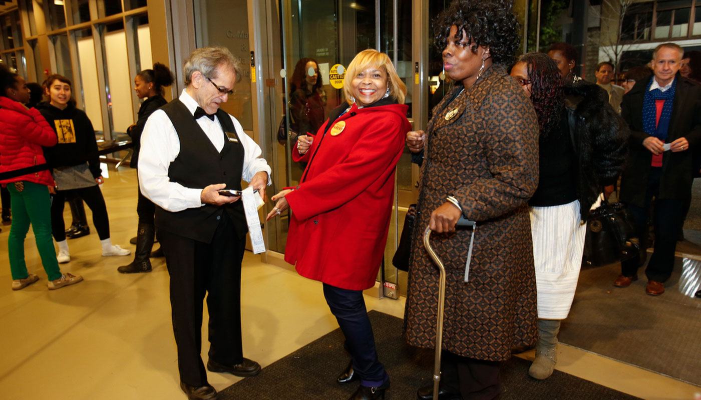 a man in a black vest and white button down scans the tickets of two women outside the theater