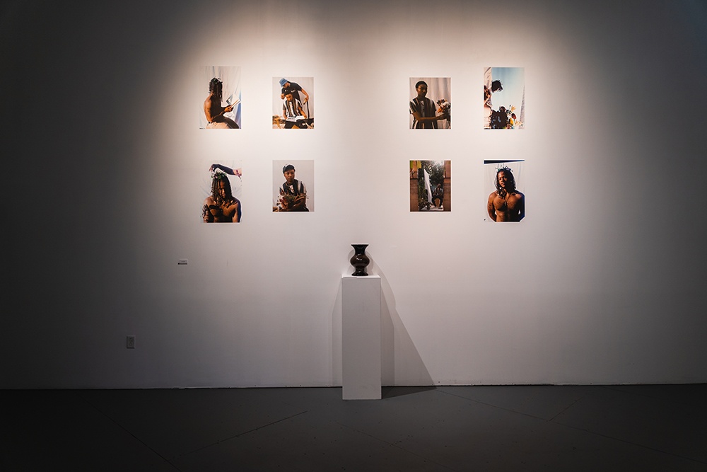 eight photograph prints hand on a white wall. a brown vase stands on a plinth in front of them