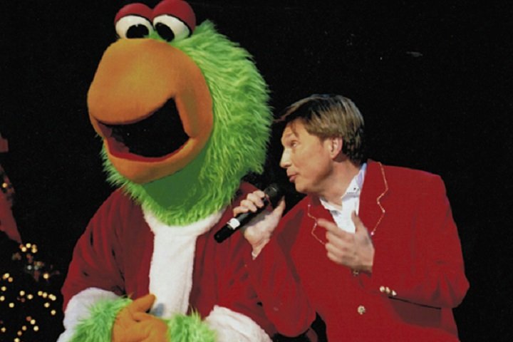 a man singing into a microphone and leaning towards a person in a fuzzy green bird costume