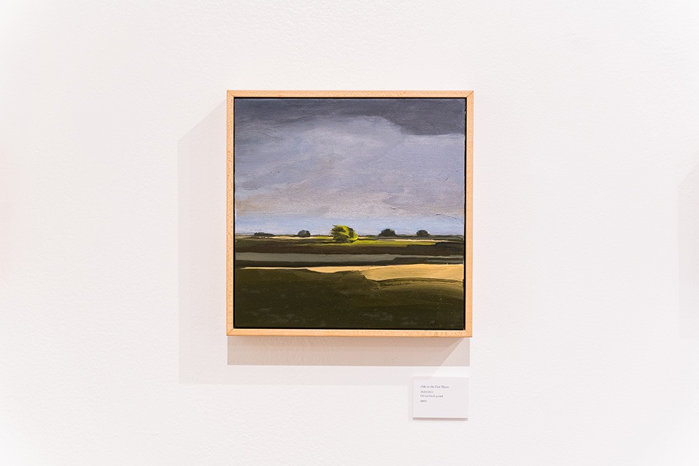 a small square painting of a country landscape hanging on a white wall