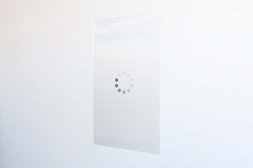 a large sheet of opaque material hangs on a white wall. a circular loading symbol is in its center