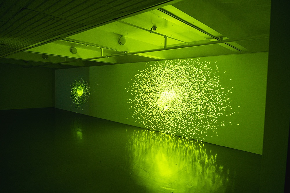 two exploding spheres of green light are projected on a long gallery wall