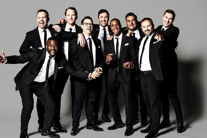 Nine men in black suits and black ties smile for a group photo.