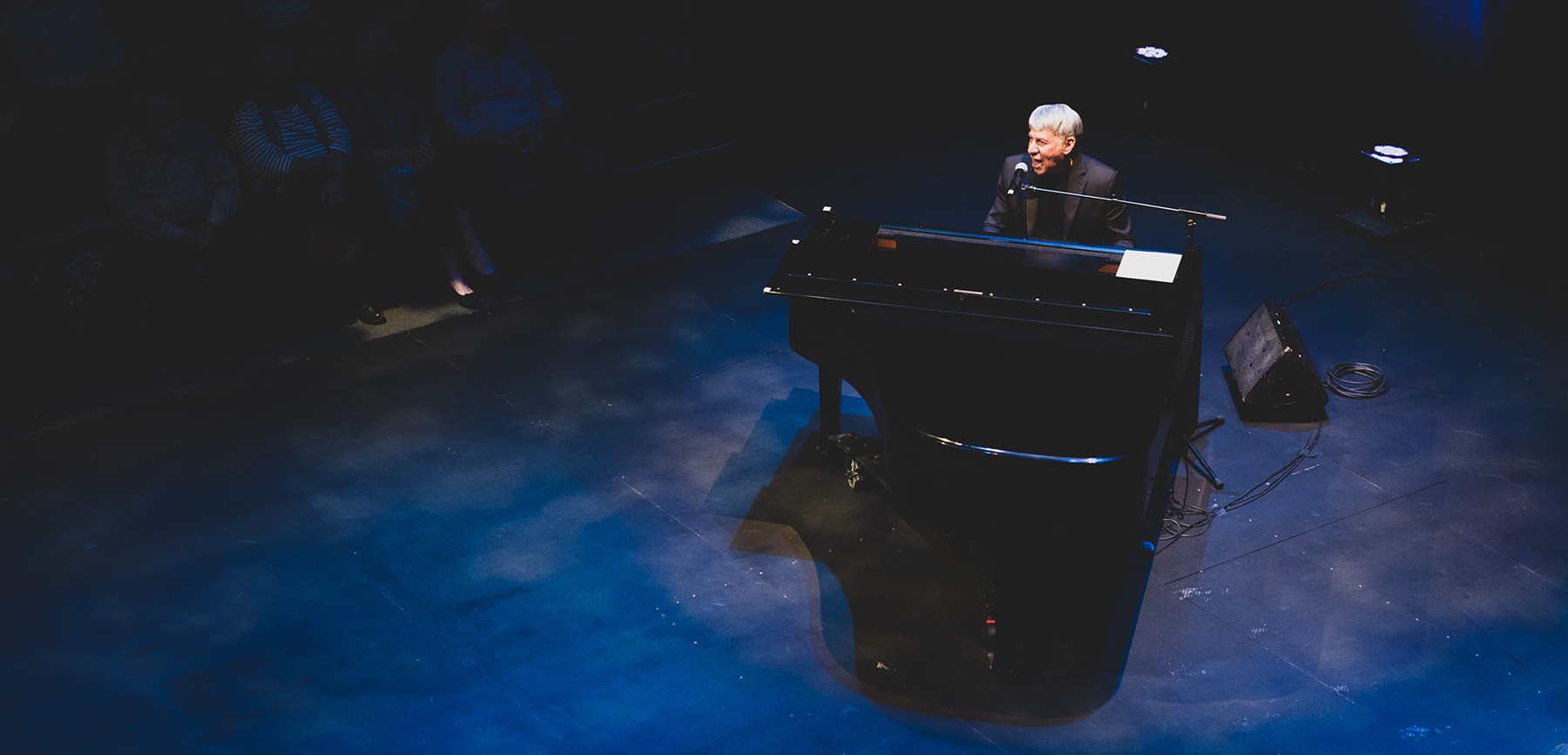 a performer sits at a grand piano and sings into a microphone