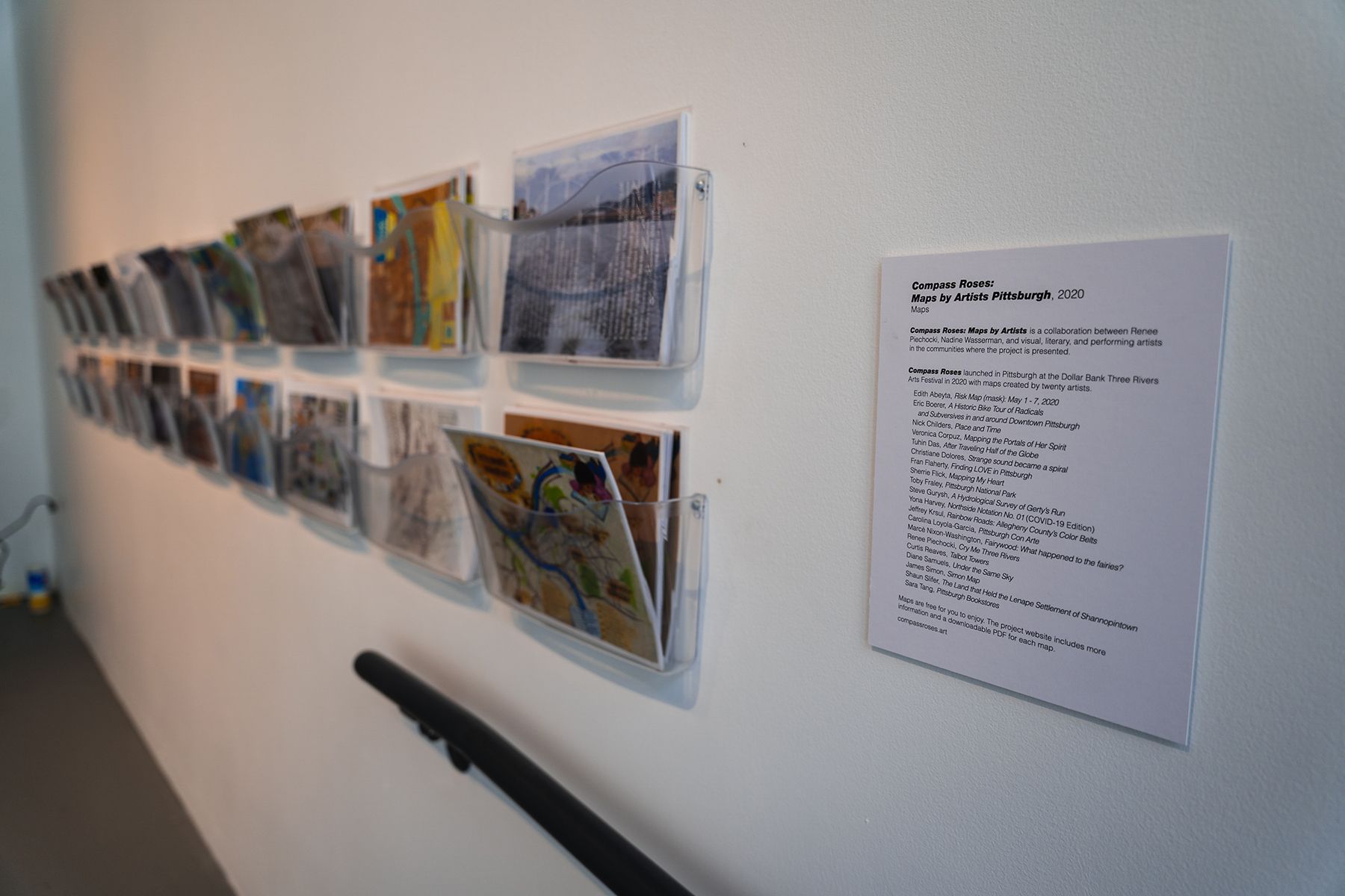 a two long rows of racks hanging on a gallery wall hold printed and laminated maps.