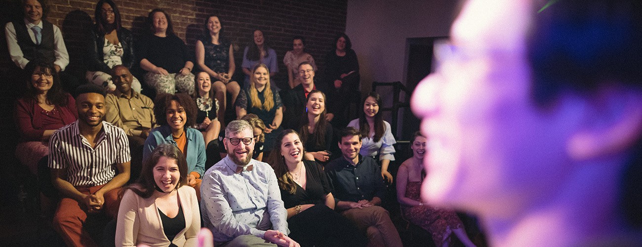 a crowd of people in the liberty magic theater, all smiling and looking at a magician on stage