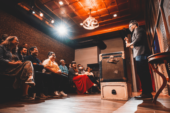 A seated group of people watch a magician on stage at Liberty Magic.