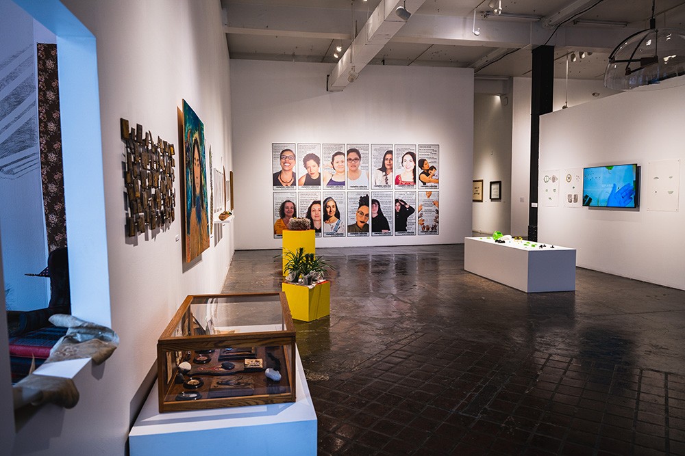 a large gallery space. 14 posters hang on a far wall with photo portraits printed on them.
