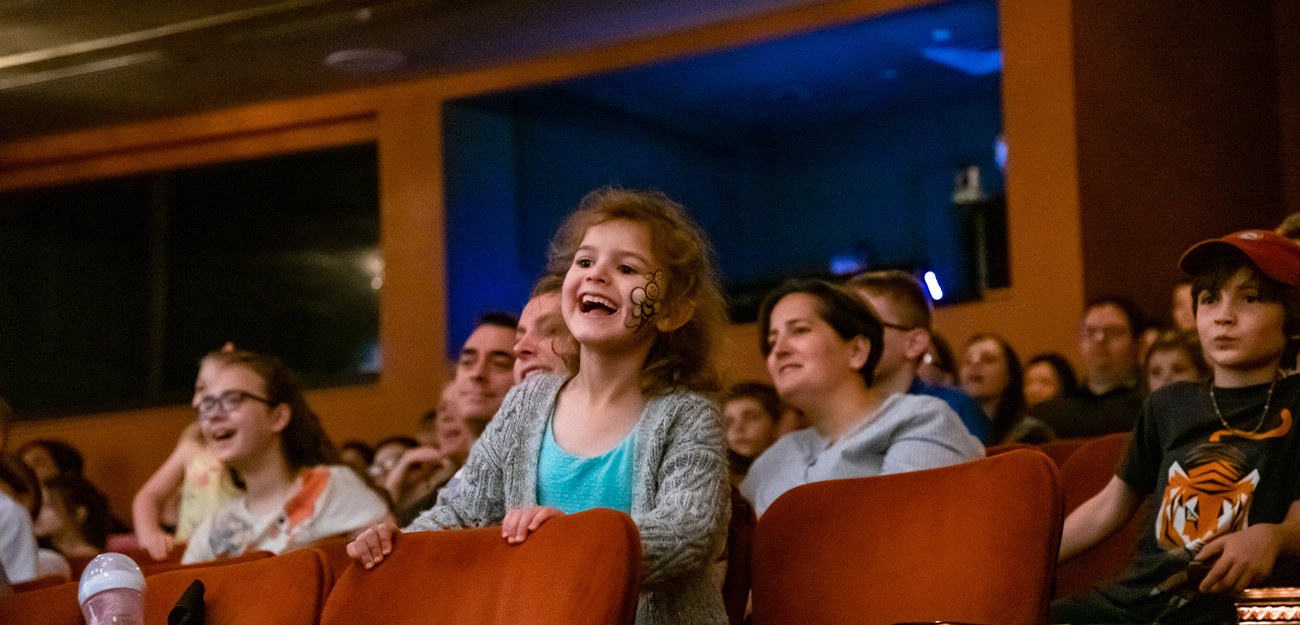 A child sitting in a theater seat smiling.