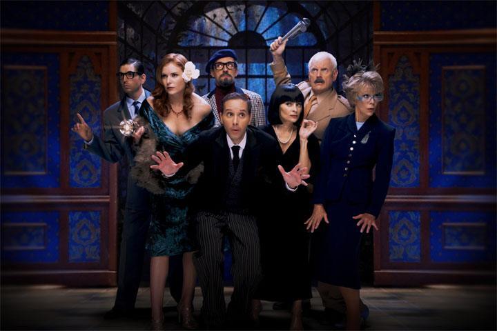 Three women and four men in cocktail attire stand together but look in different directions with a paneled, patterned wall behind them.