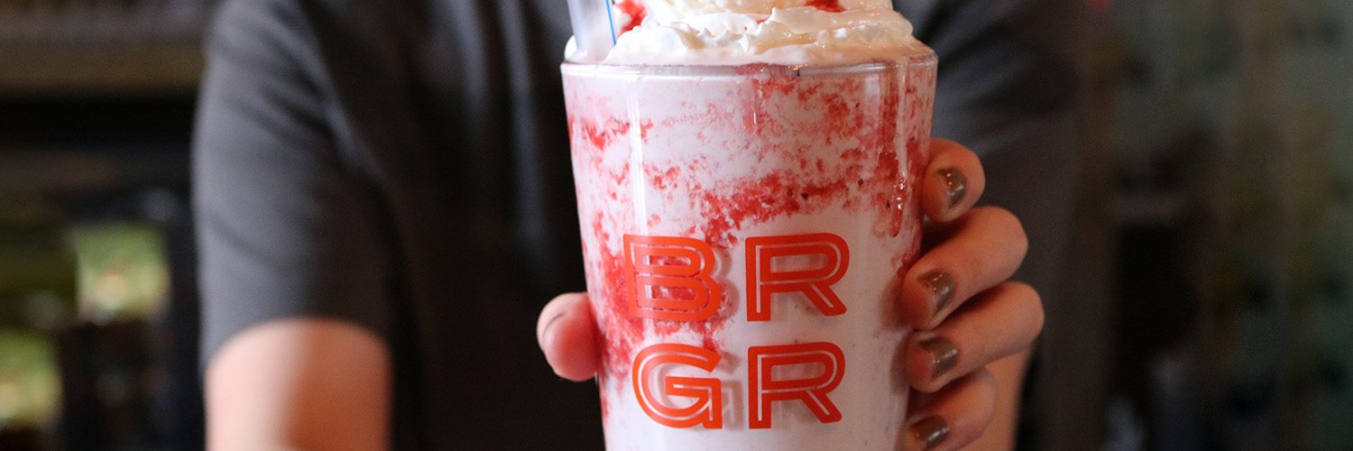 a pink milkshake in focus with whip cream on top of it. text on the glass reads: BRGR