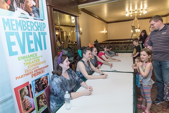 kids stand in line with their parents to meet costumed cast members behind a table