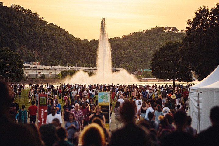 the sun sets over a crowded point state park during the dollar bank three rivers arts festival