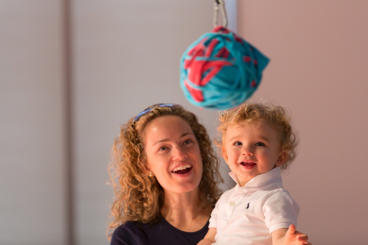 a mom holds her baby, who is fascinated by a toy in front of him