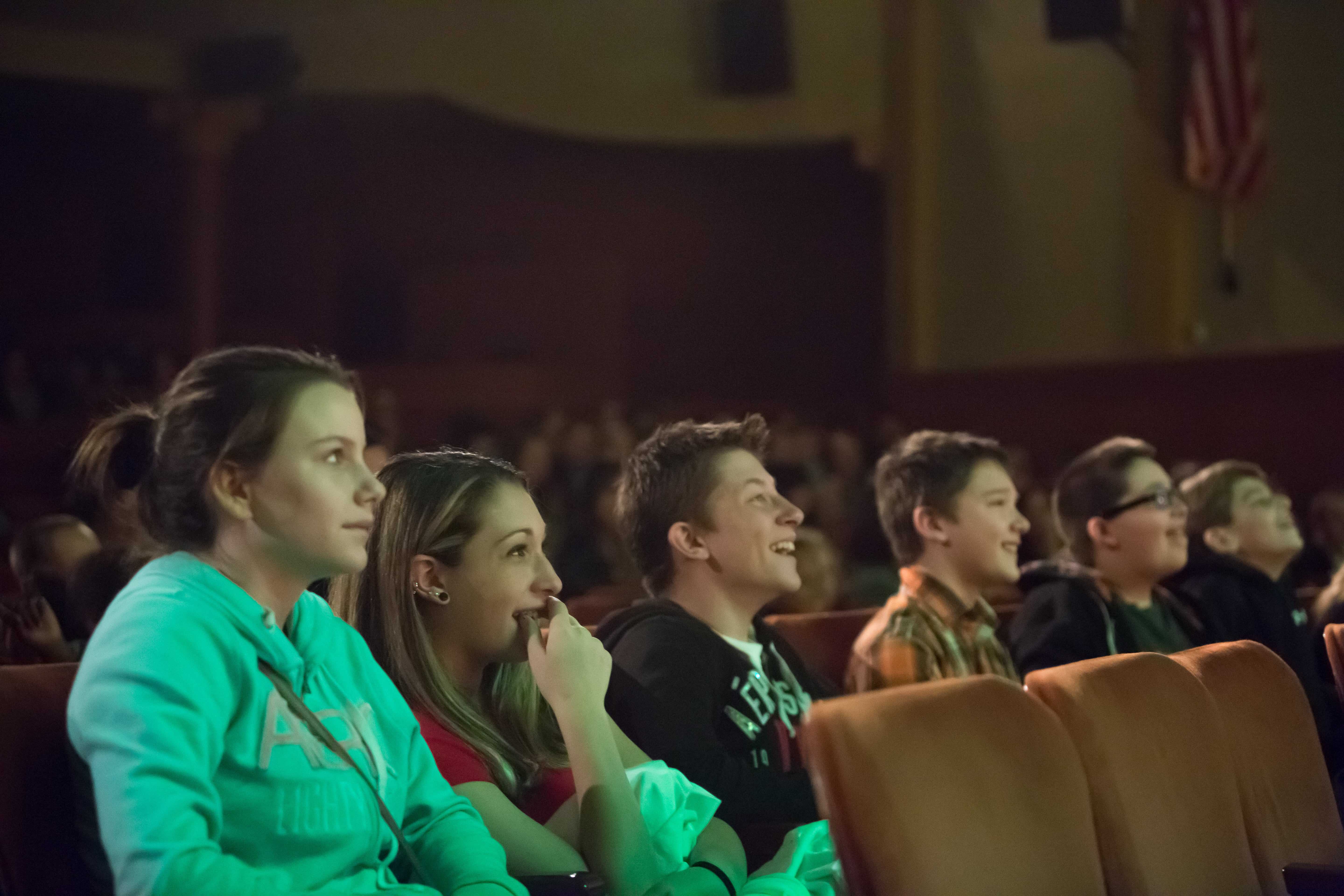 a group of teens sit in a theater enjoying a show