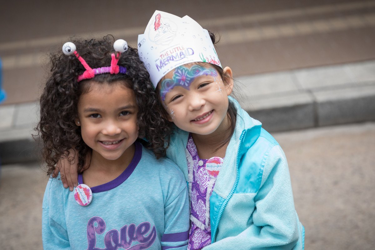 two young girls smile at the camera. their faces are painted and they wear handmade headbands and crowns