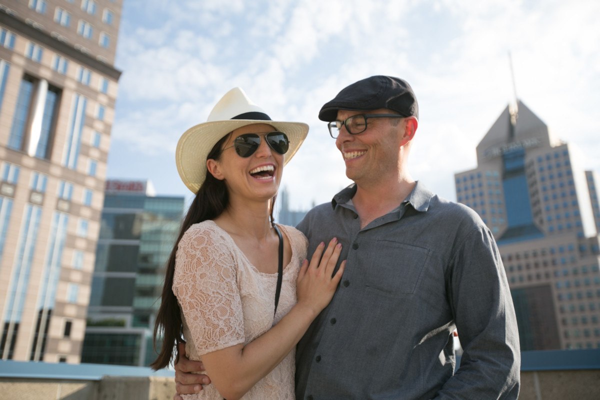 couple laughs and smiles while standing on downtown pittsburgh rooftop