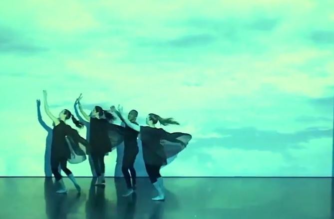 four dancers in black in front of blue screen