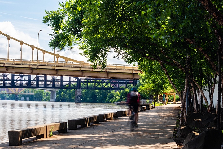 A biker rides on the Allegheny Riverfront Park path towards the convention center