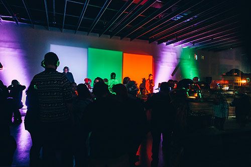 group of people dancing in a room with multicolor lights projected behind them