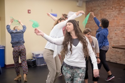 woman holding small silk scarf above her head, other women behind her are doing similar motions