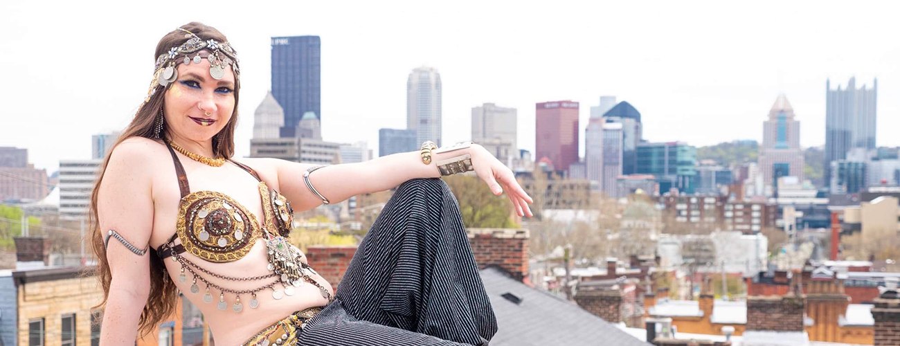 belly dancer sitting down on a wall with Pittsburgh skyline behind her