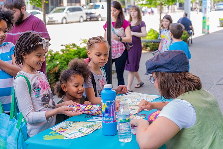 a group of children presenting their completed frog stop sheets to a festival guide