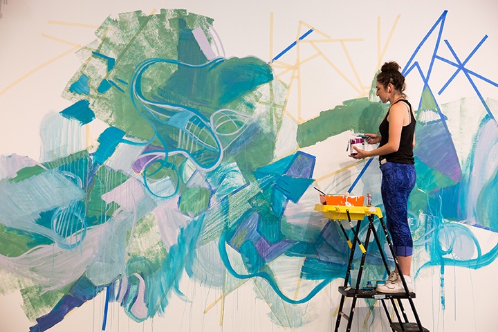 a photo of a person standing on a ladder painting a mural on a wall