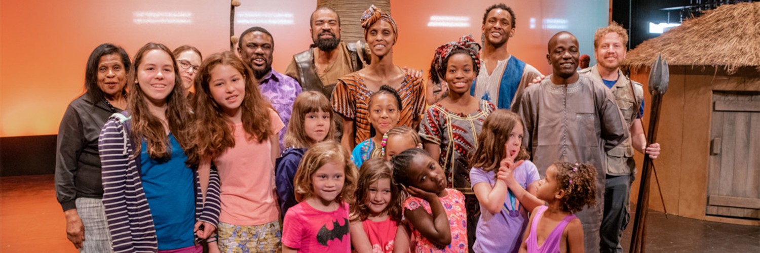 Group of young girls with performers, smiling for a picture after a show.