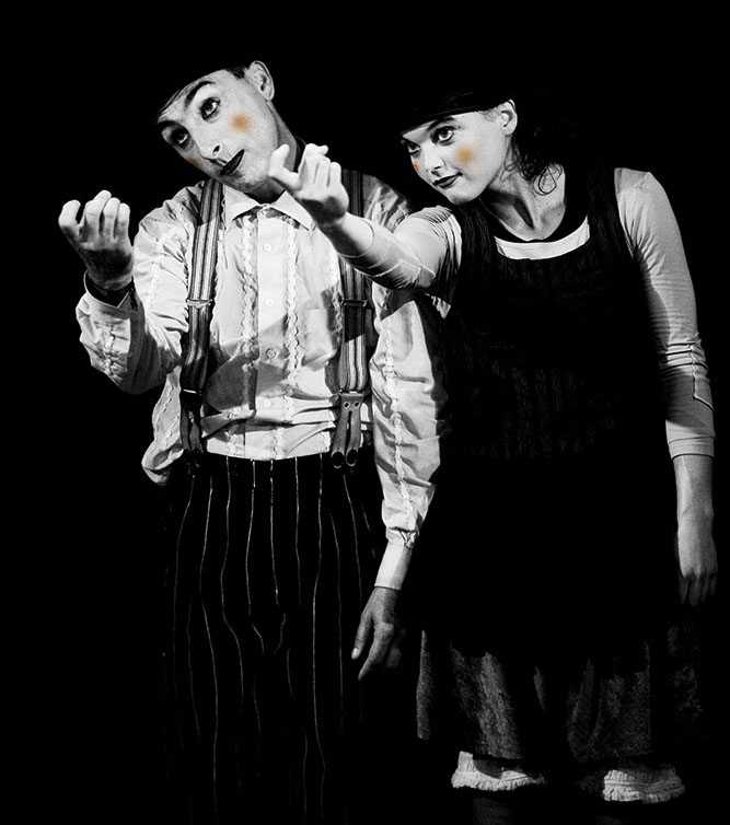 A male and female acrobat with stage makeup on summon an unseen audience with their fingers