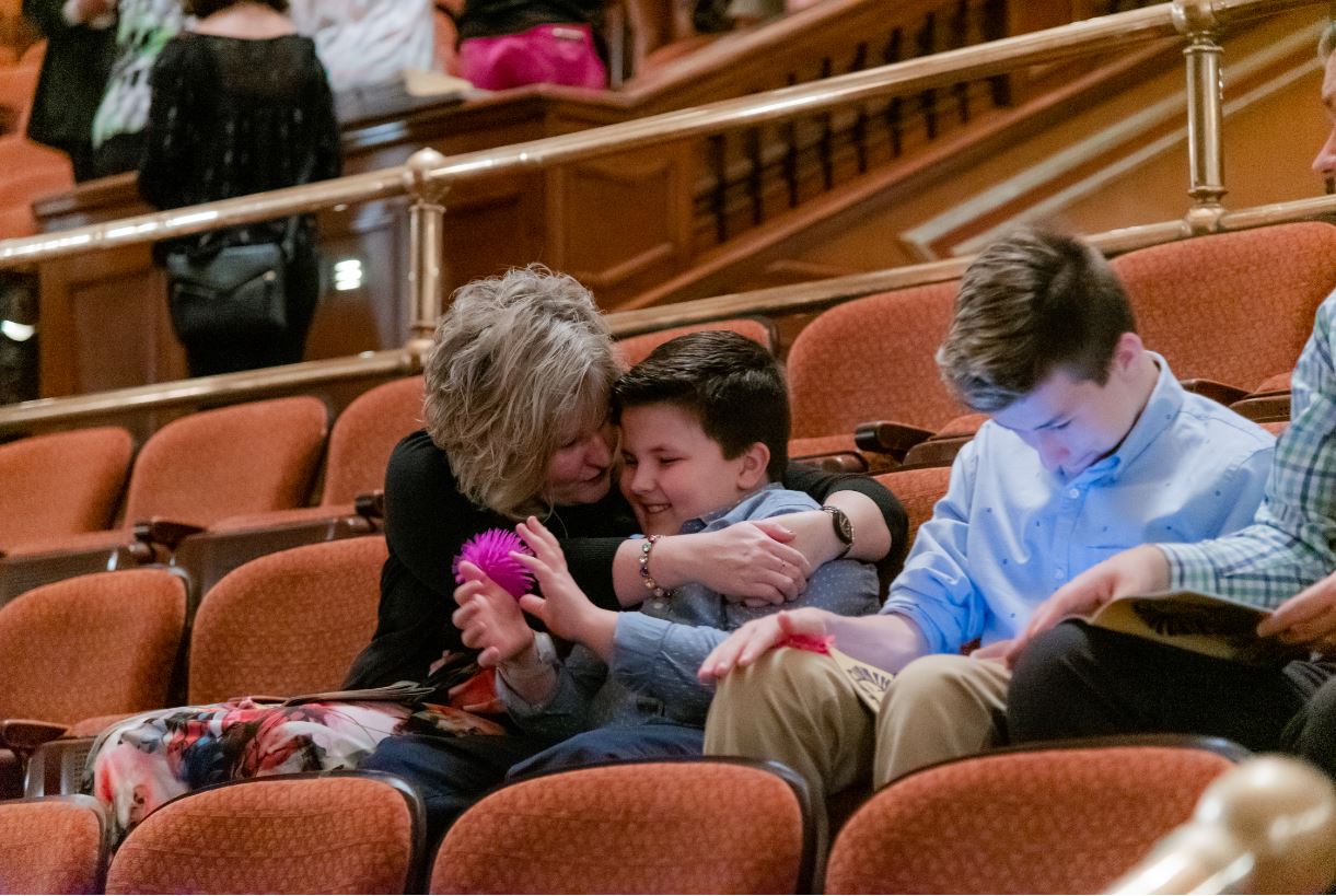 Kid smiling and playing with stress ball in the theater while mother hugs son