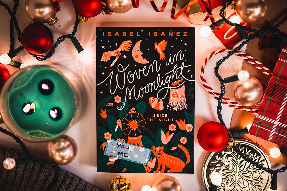 a photo of Isabel Ibañez's book 'woven in moonlight' surrounded by holiday decorations