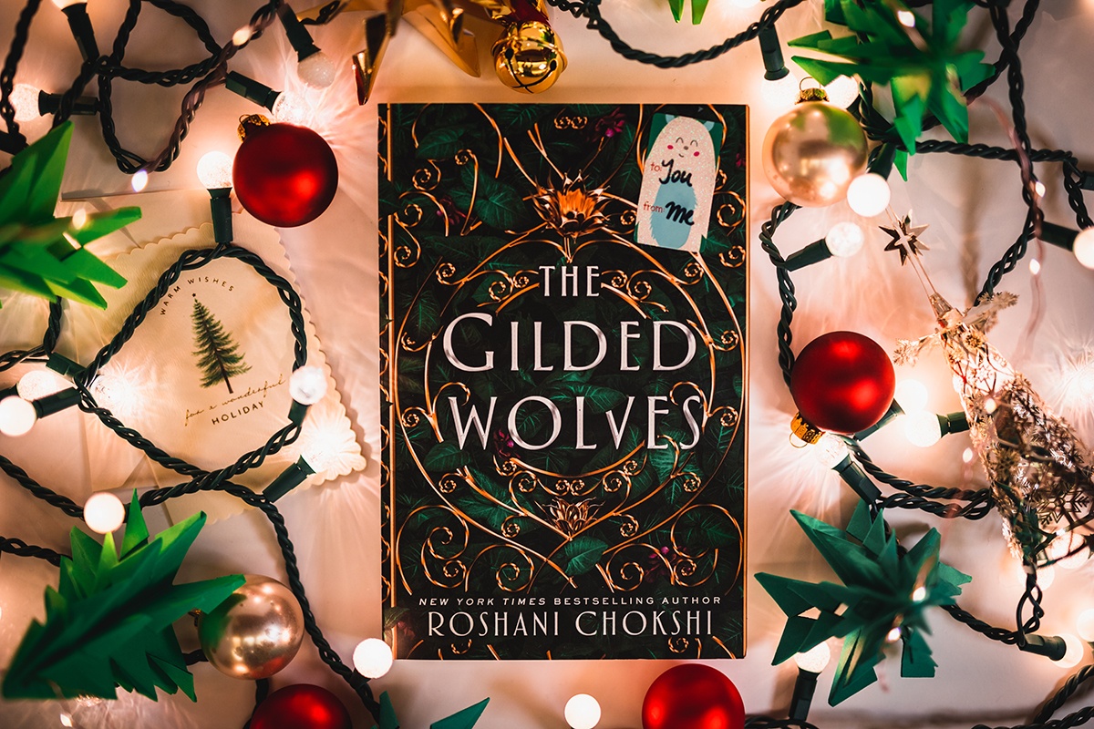 a photo of Roshani Chokshi's book 'the gilded wolves' surrounded by holiday decorations