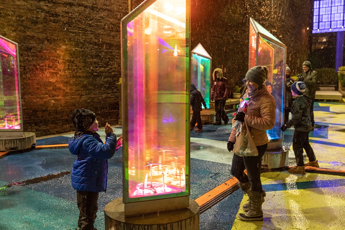 an adult and a child interact with the spinning, light-up prisms as part of the Prismatica installation