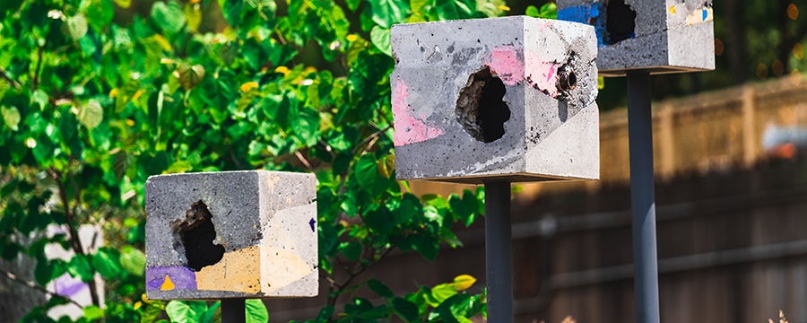 three concrete birdhouse boxes with green trees behind them