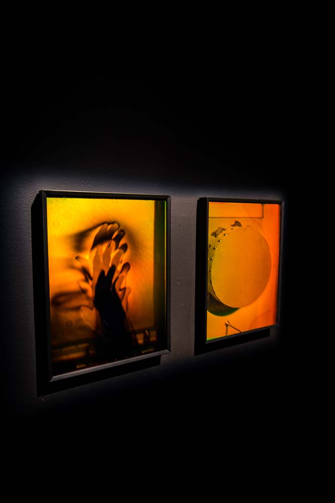 Two yellow and orange holograms that are part of Gift Shop. One is the dark blurred imprint of a moving hand and the other is a tambourine