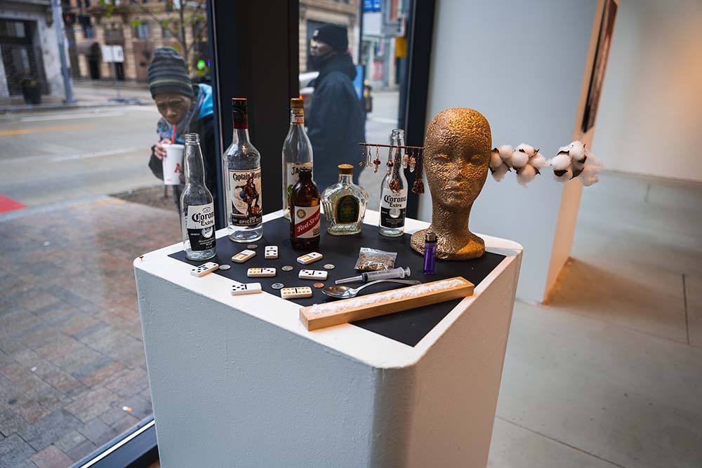 A pedestal displaying a collection of items - alcohol bottles, dominoes, and drug paraphernalia
