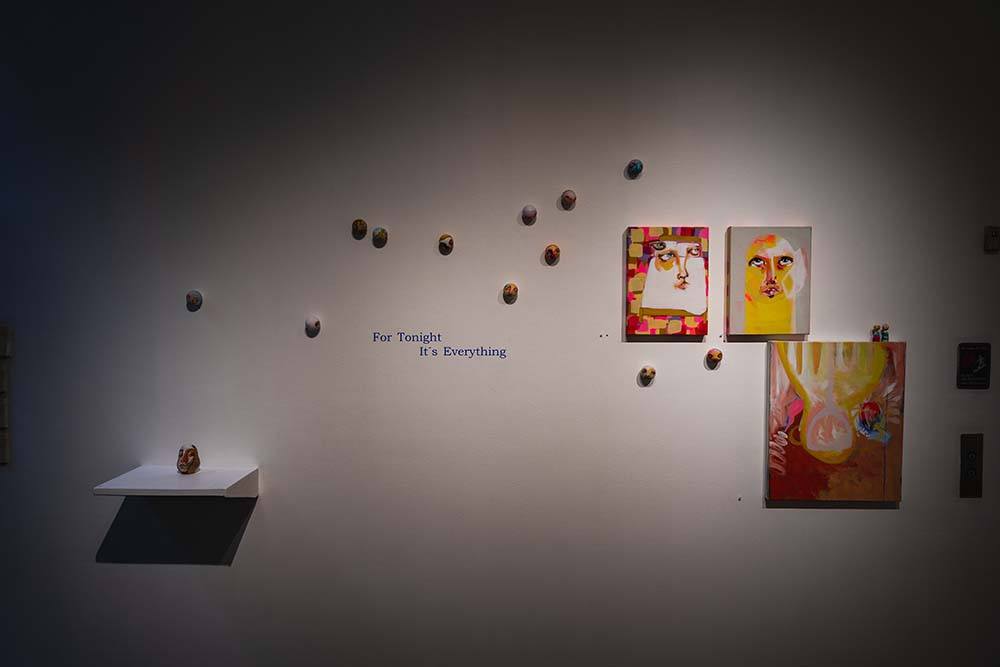 A gallery wall hung with three abstract paintings and a dozen small painted wooden balls