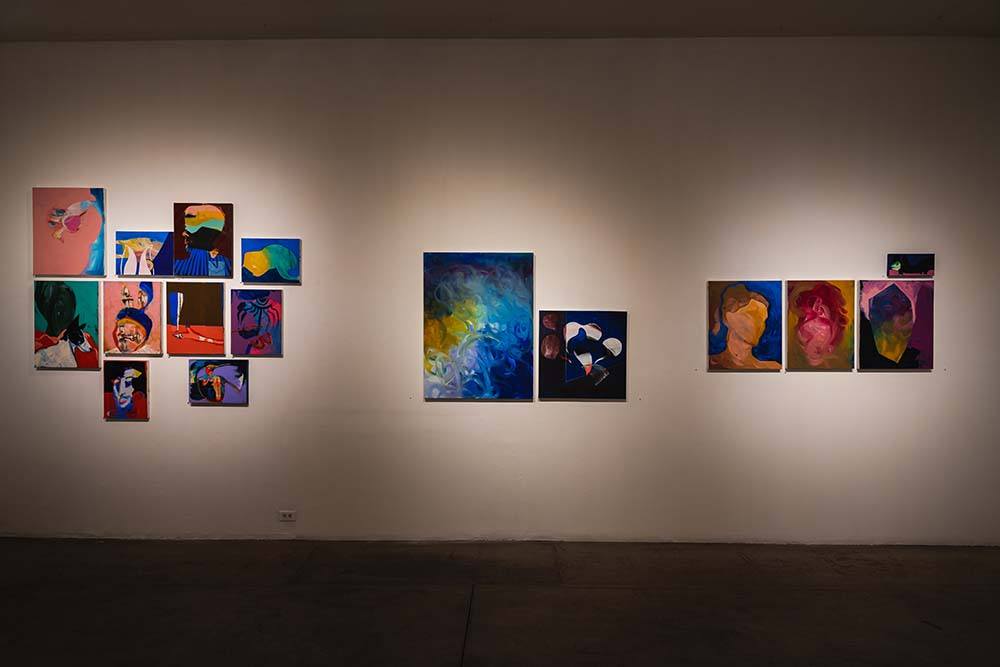 A gallery wall with 16 multicolored abstract paintings on it