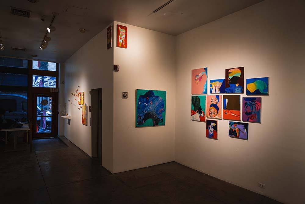 A wide view of three gallery walls, all with multicolored abstract paintings on them