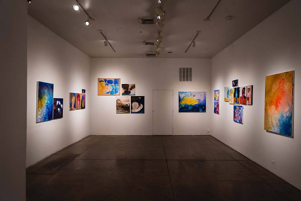 A wide view of the gallery, with abstract paintings of varying sizes on three walls