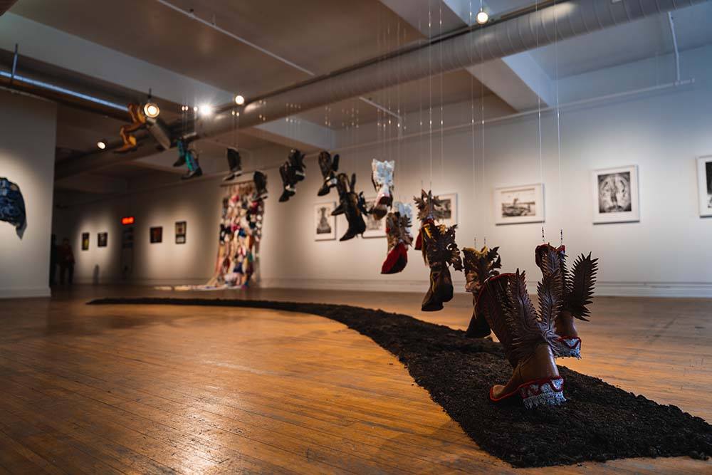 A piece made up of many pairs of cowboy boots hanging from clear thread, meant to depict them stepping up into the air