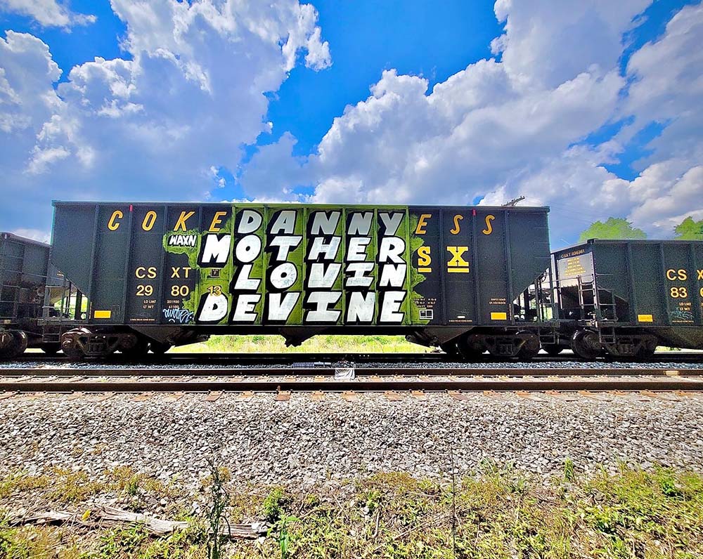 the words 'danny mother lovin devine' spray painted in bubble letters on a rail car